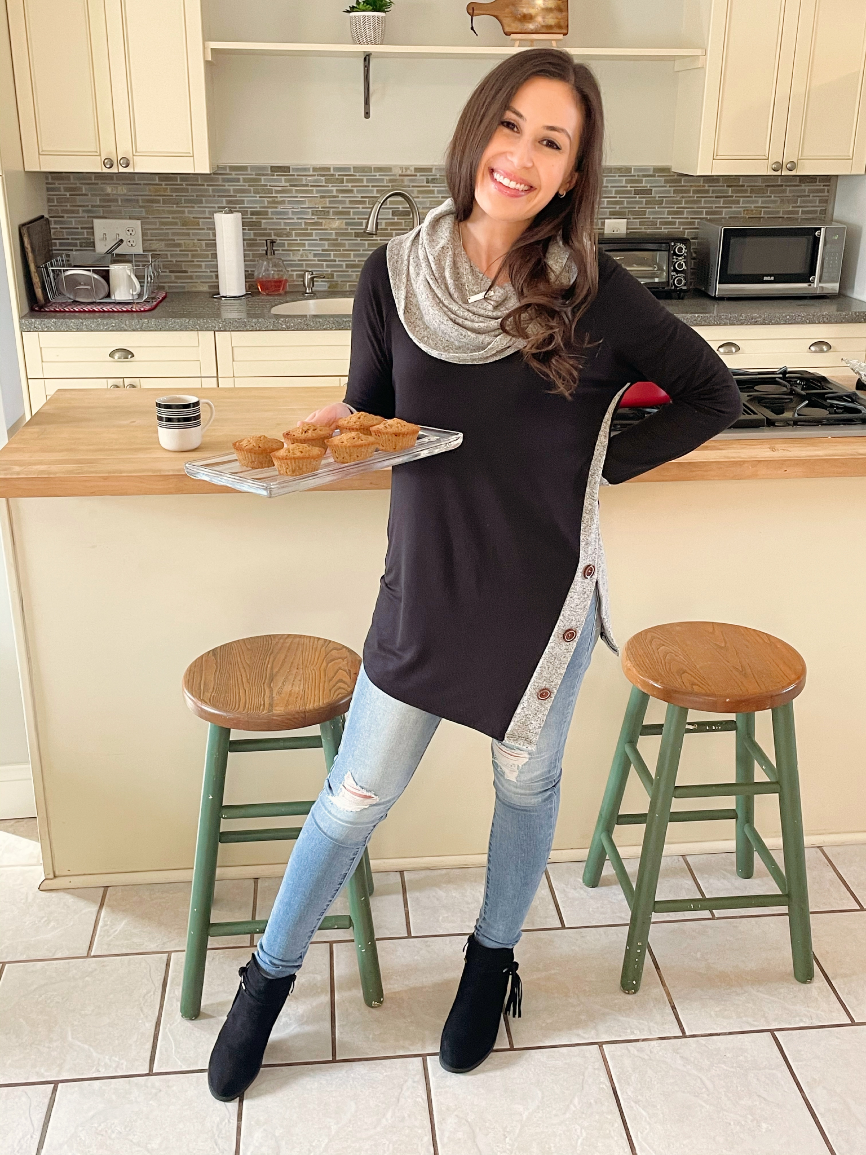 young stylish woman holding tray of muffins in boho kitchen